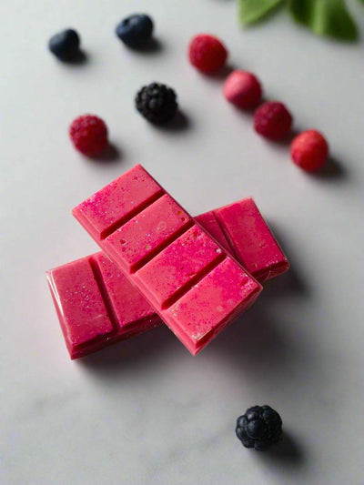 Pink wax melt snap bars with a berry scent theme, surrounded by assorted fresh berries on a light surface.